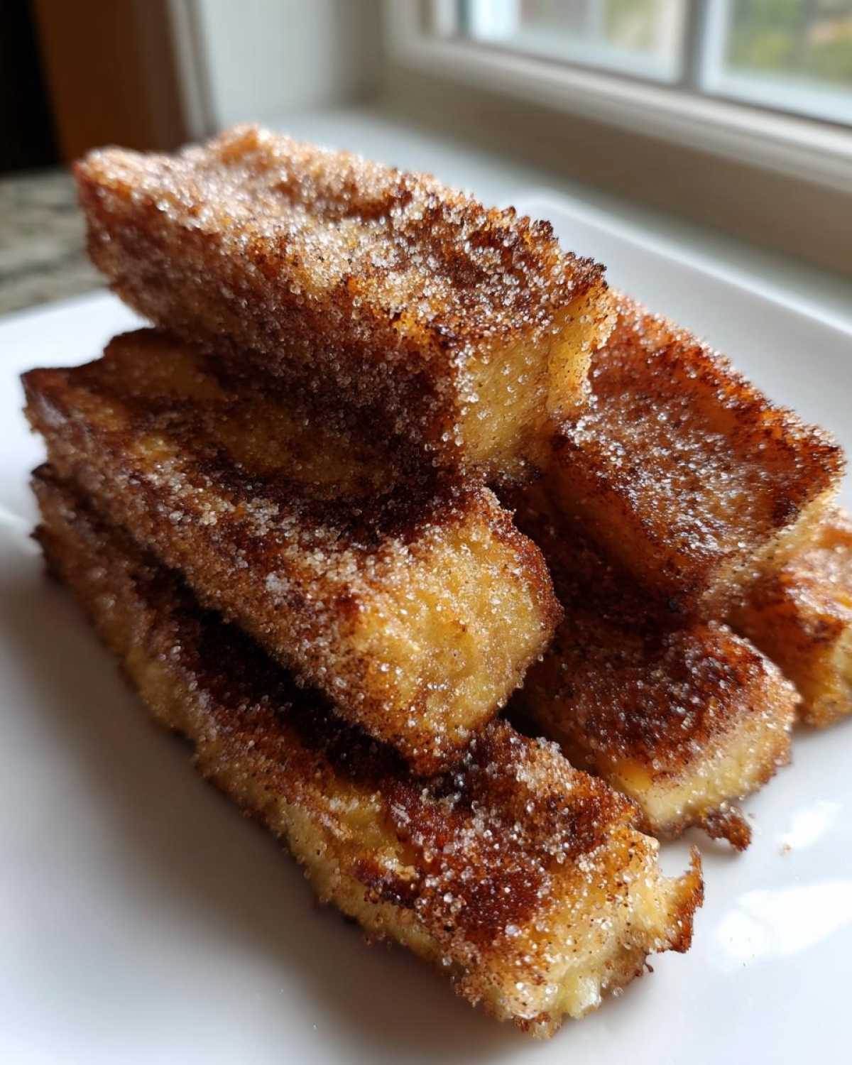 A stack of golden Air Fryer French Toast Sticks heavily coated in sparkling cinnamon sugar.