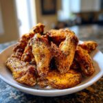 A close-up of crispy, golden Air Fryer Lemon Pepper Wings piled high on a white serving dish.