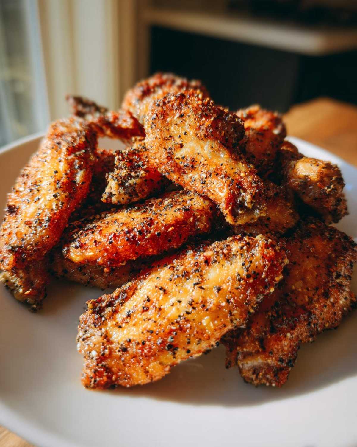 A close-up pile of crispy, seasoned Air Fryer Lemon Pepper Wings on a white plate.