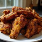 A pile of crispy, golden brown Air Fryer Lemon Pepper Wings seasoned heavily with black pepper, served on a white plate.