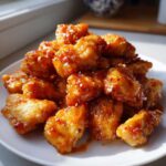Close-up of crispy, glazed pieces of Air Fryer Orange Chicken piled on a white plate, sprinkled with sesame seeds.