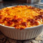 A close-up of a freshly Baked Buffalo Chicken Dip in a white ceramic dish, featuring a bubbly, golden-brown melted cheese topping.