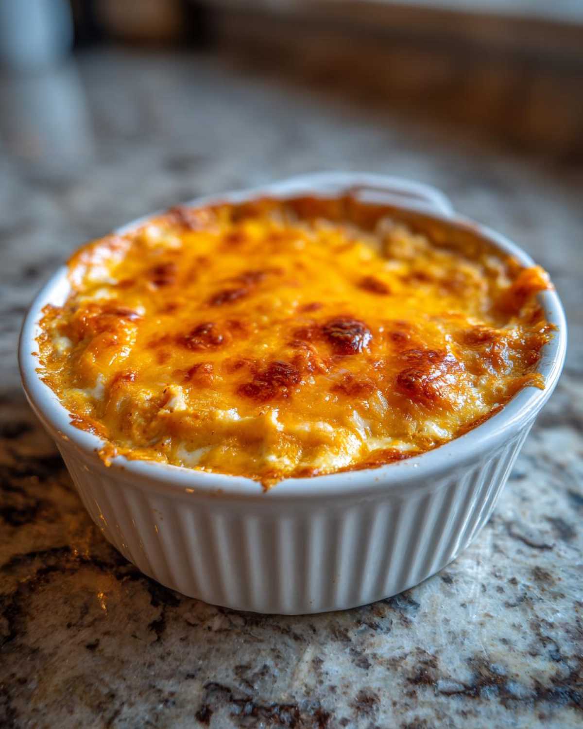 Close-up of hot Baked Buffalo Chicken Dip with melted, browned cheese topping in a white ramekin.