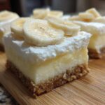 Close-up of a layered Banana Pudding Cheesecake Bars slice with graham cracker crust, creamy filling, whipped topping, and fresh banana slices.