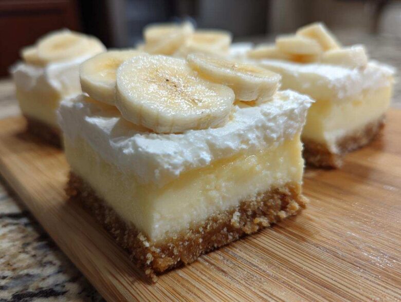 Close-up of a layered Banana Pudding Cheesecake Bars slice with graham cracker crust, creamy filling, whipped topping, and fresh banana slices.