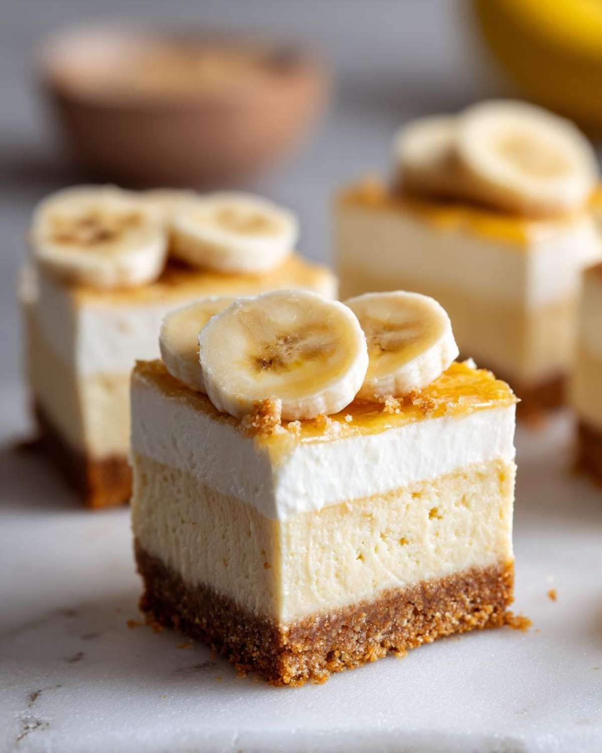 Close-up of a square serving of Banana Pudding Cheesecake Bars showing three layers, topped with white cream, glaze, and fresh banana slices.
