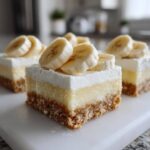 Close-up of three layered Banana Pudding Cheesecake Bars topped with fresh banana slices.