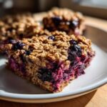 A close-up of a thick, moist square of Blueberry Baked Oatmeal Squares showing the rich berry filling and oat topping.