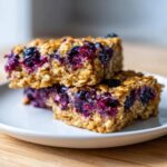Close-up of two stacked Blueberry Baked Oatmeal Squares featuring visible oats and rich purple berries.