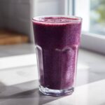 A tall glass filled with a thick, deep purple Blueberry Lemon Chia Smoothie sitting on a bright countertop.