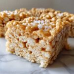 A close-up of a square Brown Butter Rice Krispie Treat Bar topped with flaky sea salt.