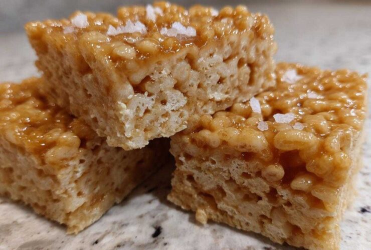 Three stacked Brown Butter Rice Krispie Treat Bars topped with flaky sea salt on a granite counter.