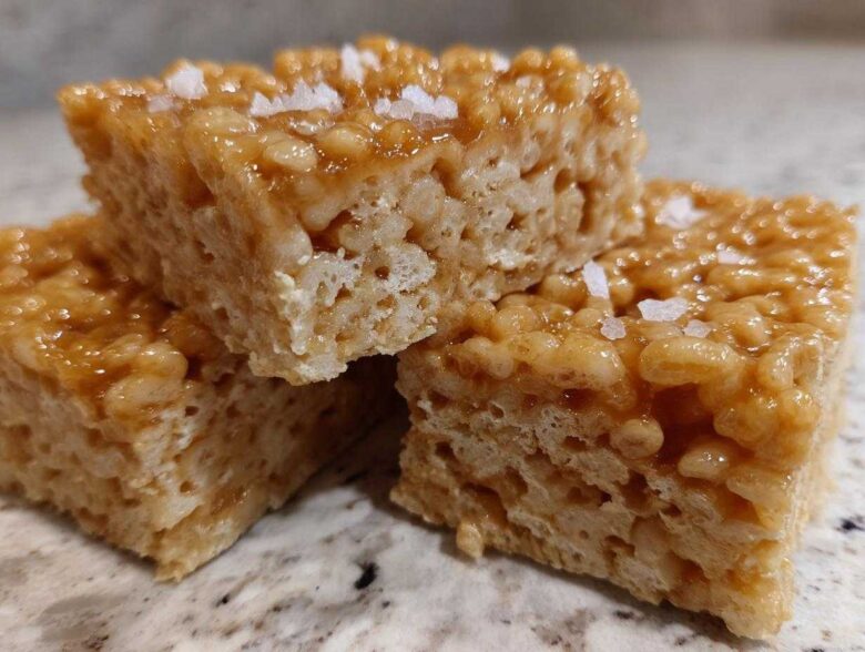 Three stacked Brown Butter Rice Krispie Treat Bars topped with flaky sea salt on a granite counter.