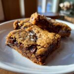 Close-up of three Chewy Chocolate Chip Cookie Bars, topped with flaky sea salt, showing melted chocolate chips inside.