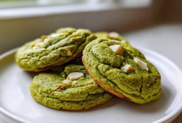 A stack of three vibrant green, chewy matcha white chocolate cookies on a white plate.