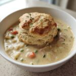 A creamy bowl of Chicken Pot Pie Soup filled with vegetables and topped with a golden biscuit.