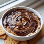 A bowl of Chocolate Peanut Butter Cheesecake Dip with a beautiful swirl of melted chocolate and peanut butter on top, served with crackers.
