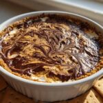 A white dish filled with Chocolate Peanut Butter Cheesecake Dip featuring a beautiful chocolate and peanut butter swirl topping and graham cracker crust.