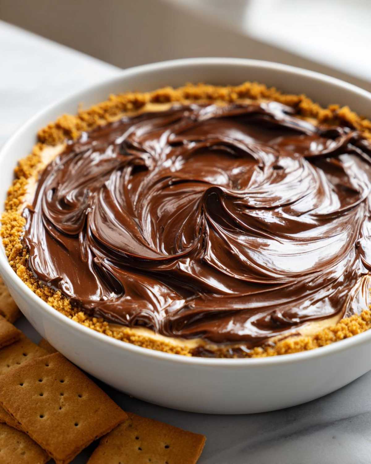 Close-up of Chocolate Peanut Butter Cheesecake Dip topped with swirled chocolate ganache and graham cracker crust.