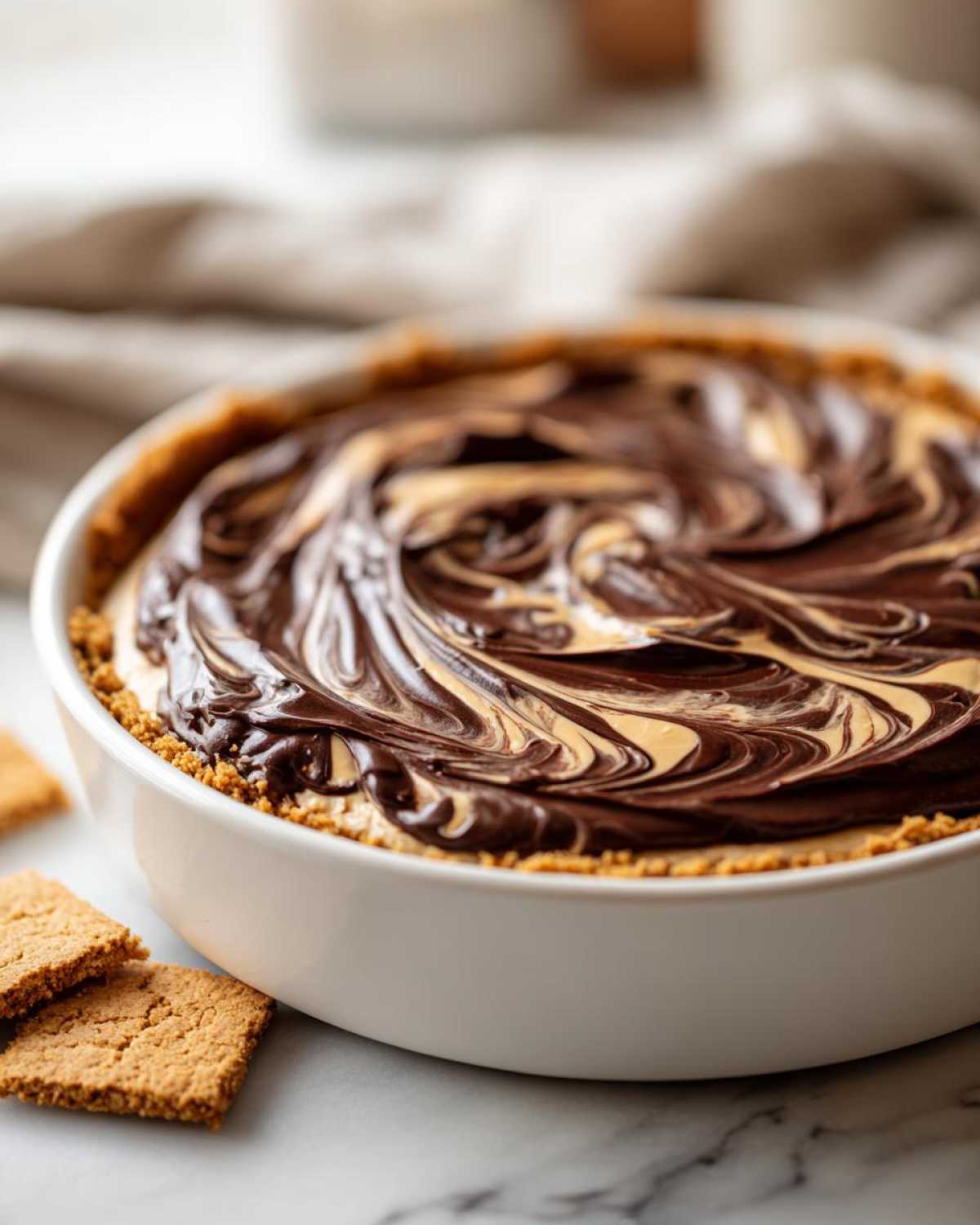 Close-up of Chocolate Peanut Butter Cheesecake Dip with swirled chocolate topping in a white dish, served with graham crackers.