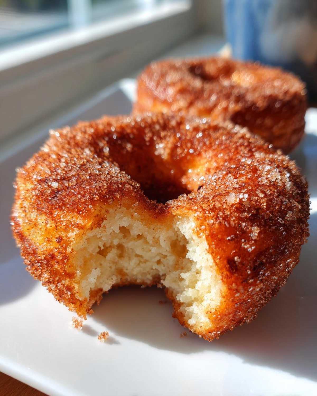 Close-up of a bite taken out of a fluffy Cinnamon Sugar Air Fryer Donut coated in sparkling sugar.