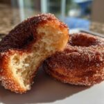 Close-up of a Cinnamon Sugar Air Fryer Donut broken in half showing the fluffy interior, next to a whole donut.