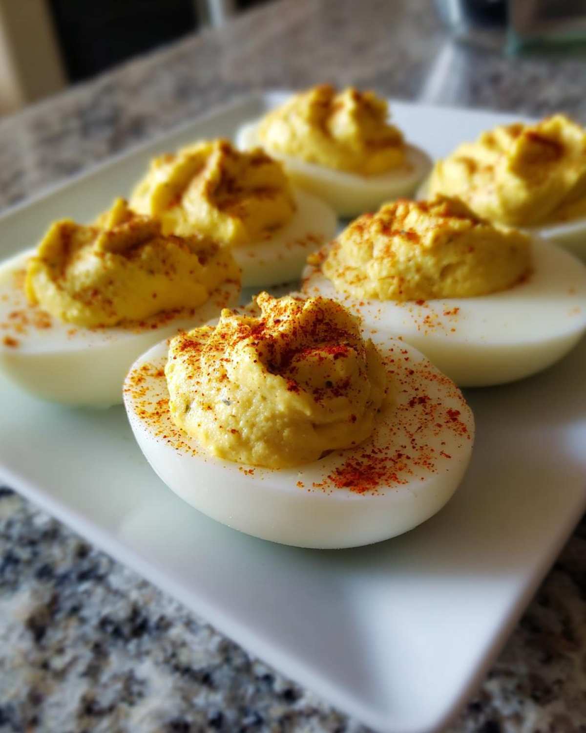 Close-up of several Classic Deviled Eggs with Dill Pickle Relish, topped with paprika, served on a white platter.