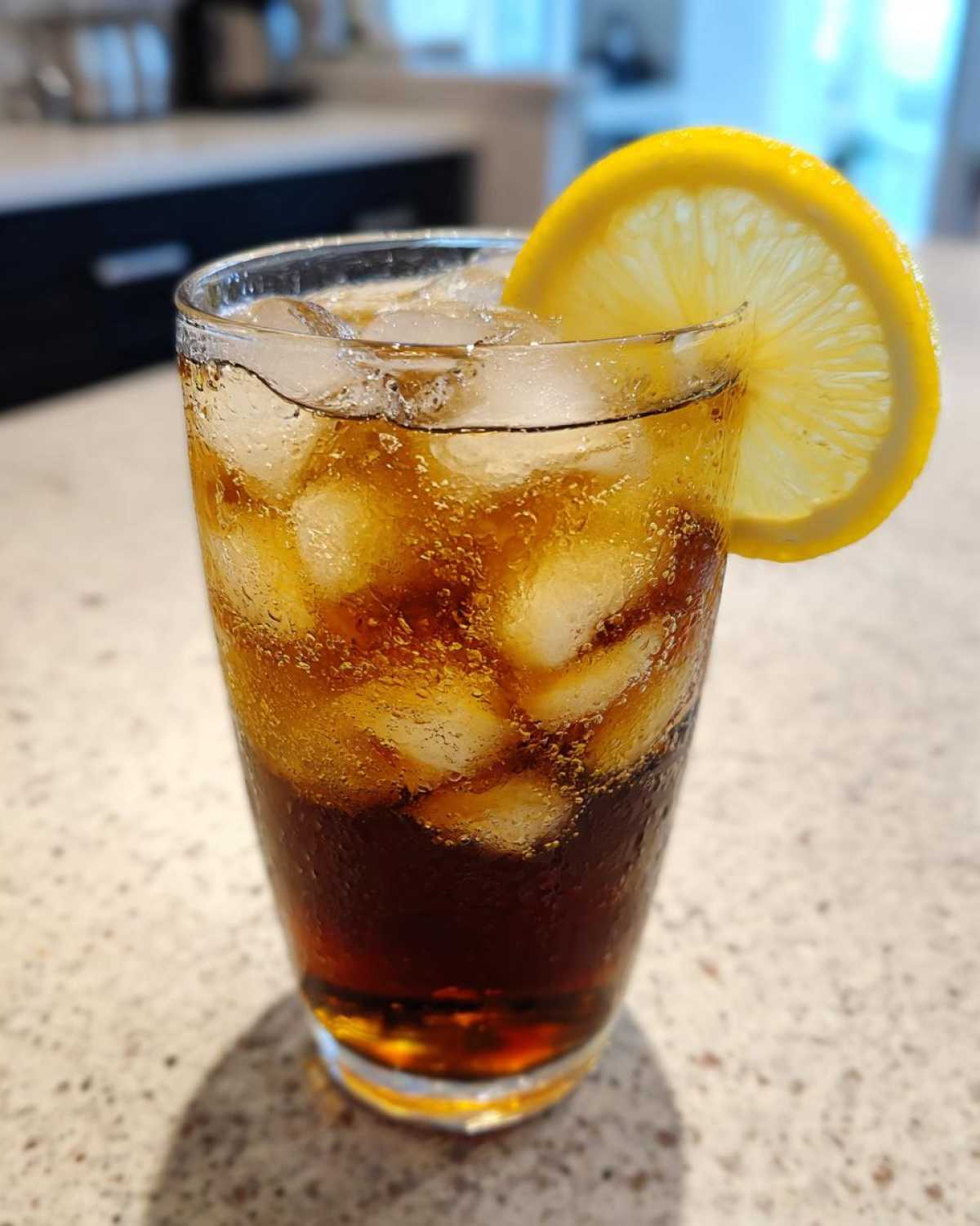 A tall glass filled with ice and dark Cold Brew Lemonade, garnished with a fresh lemon slice.