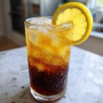 A tall, sweating glass filled with ice and layered Cold Brew Lemonade, garnished with a bright lemon slice.