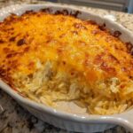 A close-up of a baked Copycat Cracker Barrel Hashbrown Casserole with a bubbly, golden-brown melted cheese topping in a white oval dish.