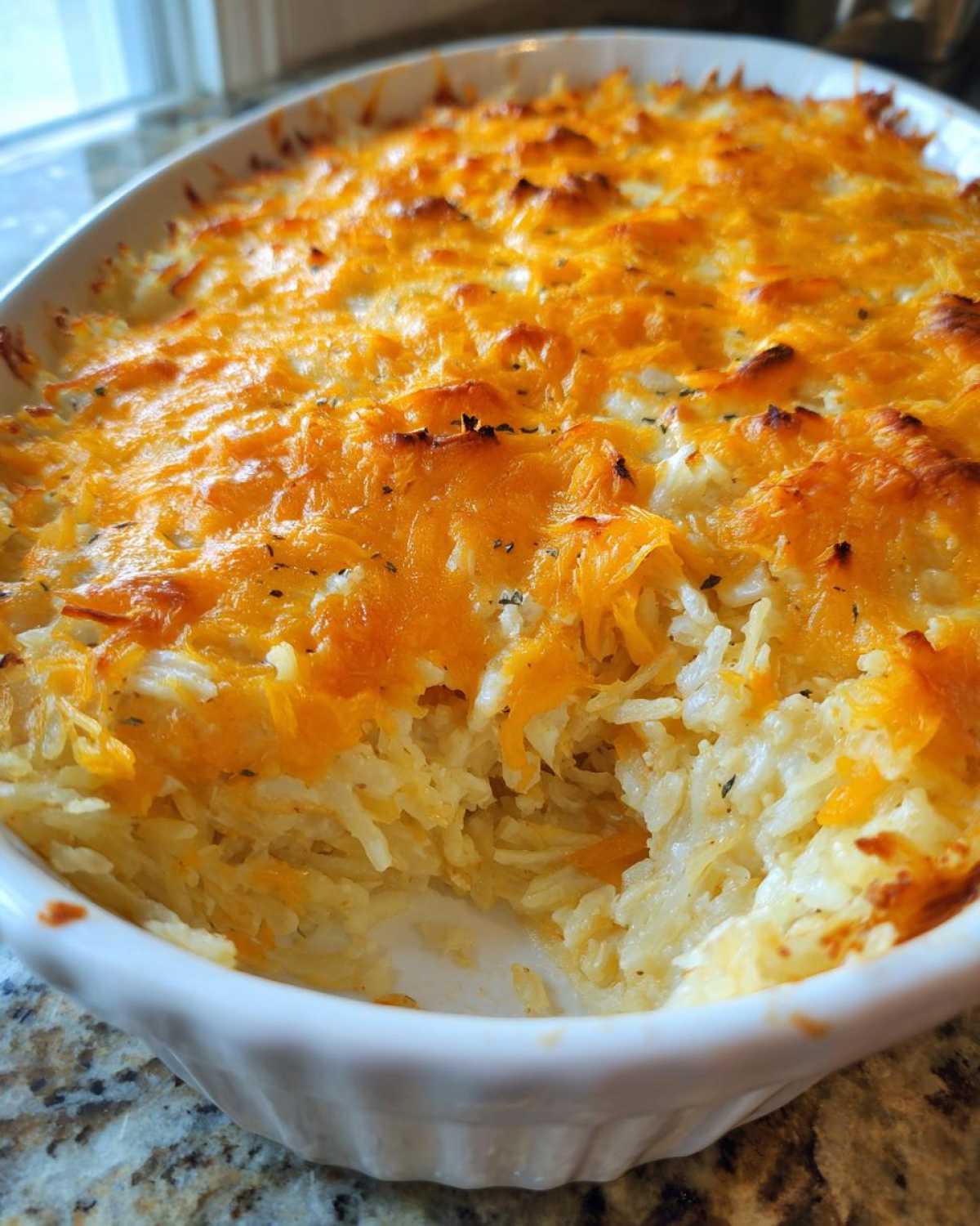 A bubbly, baked Copycat Cracker Barrel Hashbrown Casserole topped with melted, browned cheddar cheese in a white dish.