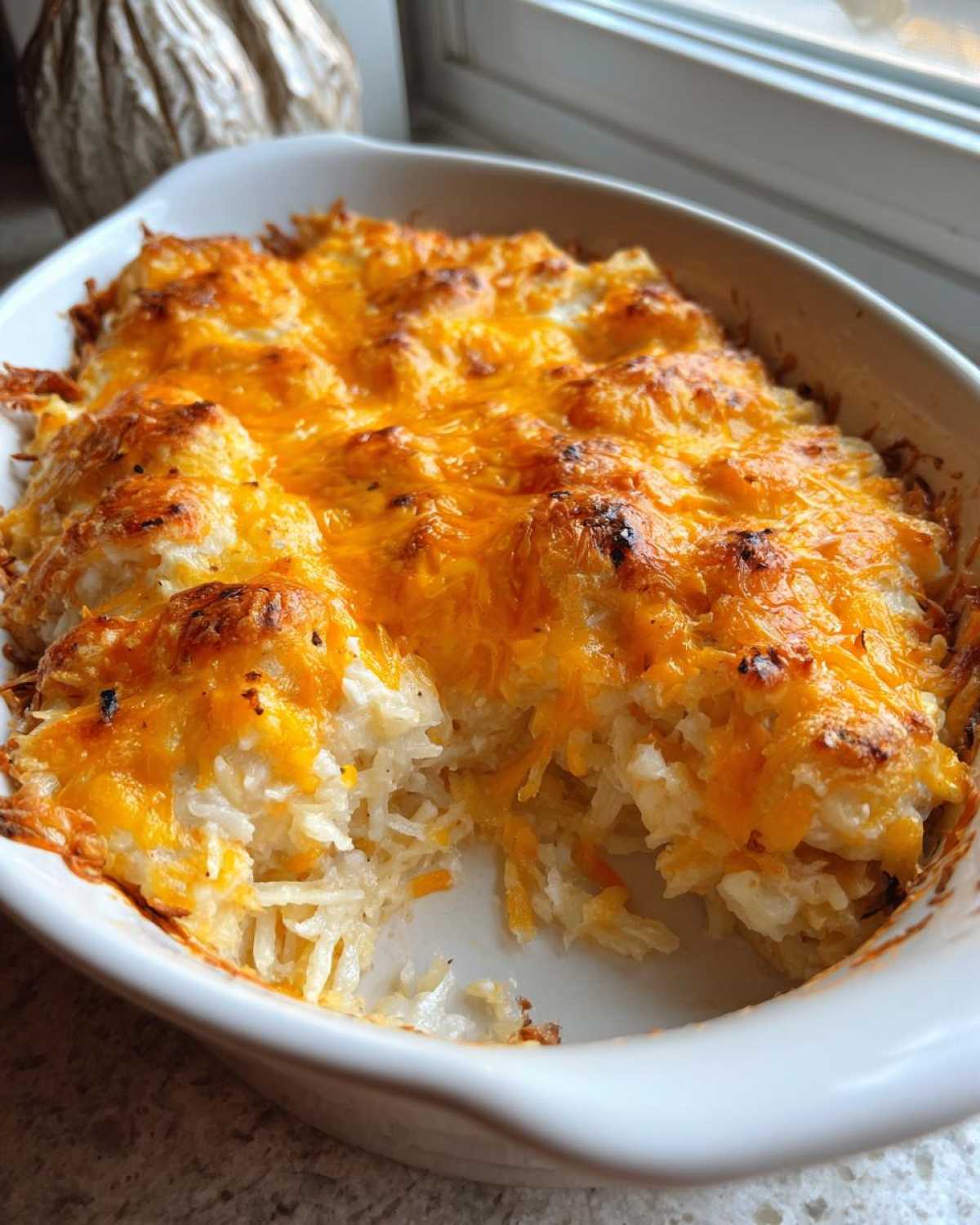 A baked Copycat Cracker Barrel Hashbrown Casserole with a bubbly, golden-brown cheddar cheese topping in a white oval dish.