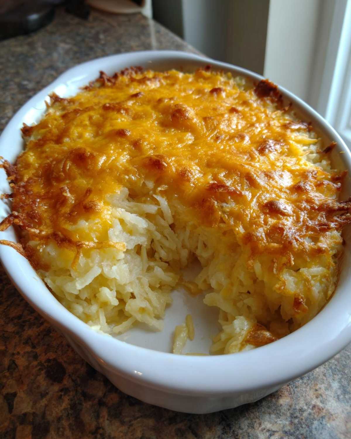 A white casserole dish filled with golden, cheesy Copycat Cracker Barrel Hashbrown Casserole, with a scoop already taken out.