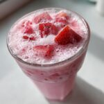 Overhead view of a frothy, pink beverage topped with strawberry and dragon fruit pieces, resembling the Copycat Starbucks Pink Drink.