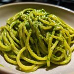 A close-up shot of thick spaghetti coated in vibrant green Creamy Avocado Pasta sauce, served in a light-colored bowl.