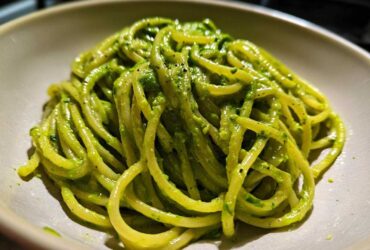 A close-up shot of thick spaghetti coated in vibrant green Creamy Avocado Pasta sauce, served in a light-colored bowl.