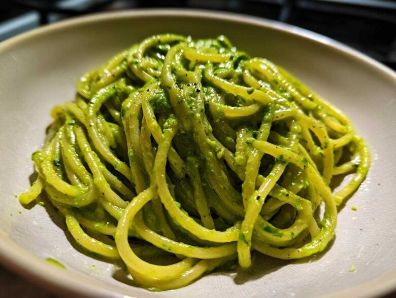 A close-up shot of thick spaghetti coated in vibrant green Creamy Avocado Pasta sauce, served in a light-colored bowl.