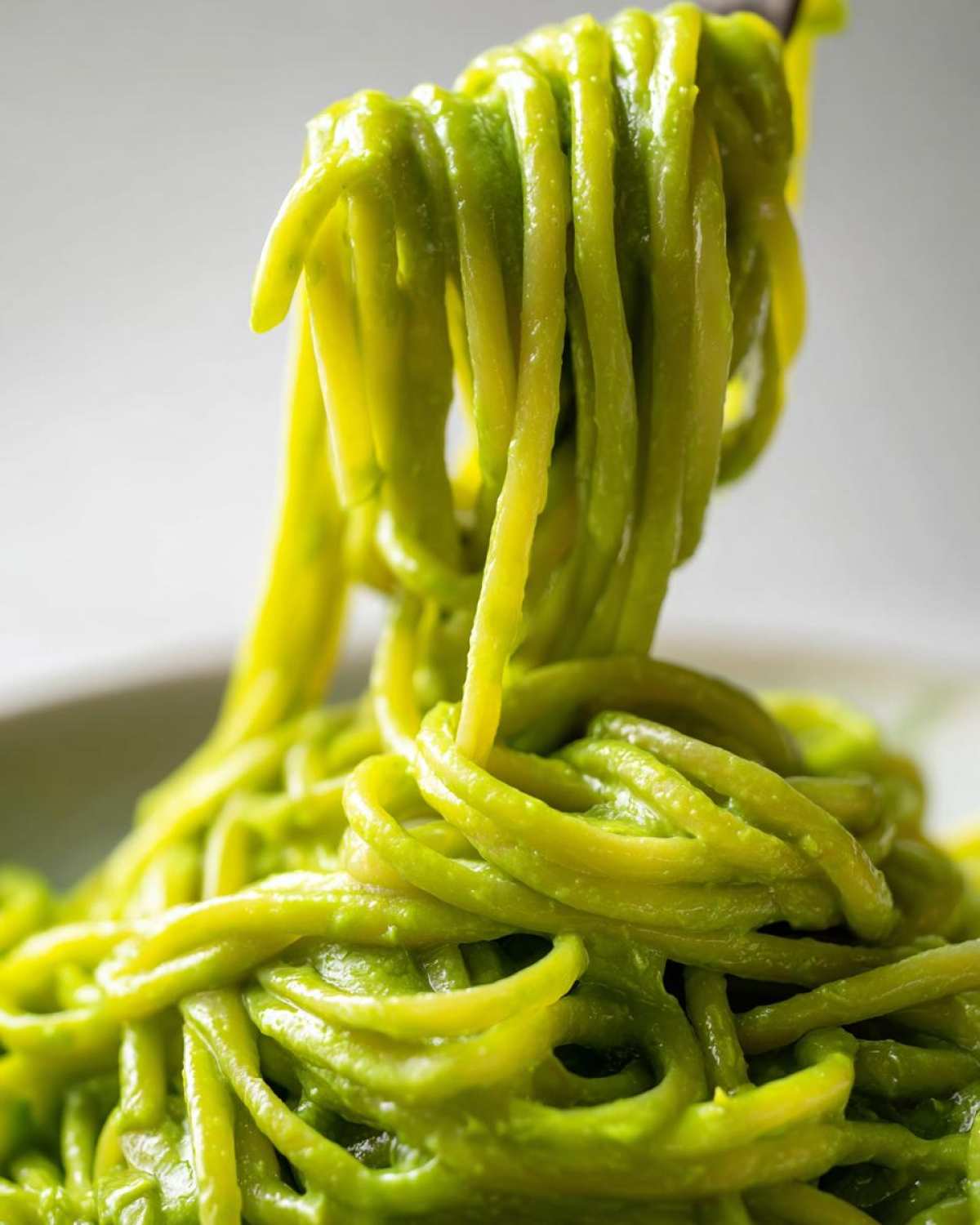 Close-up of spaghetti noodles coated in vibrant green Creamy Avocado Pasta sauce being lifted by a fork.