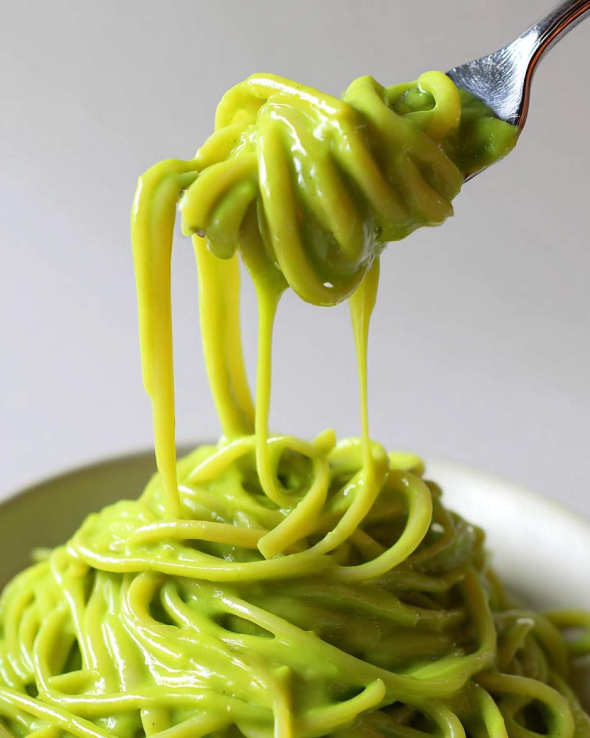 Close-up of spaghetti noodles coated in bright green Creamy Avocado Pasta sauce being lifted by a fork.