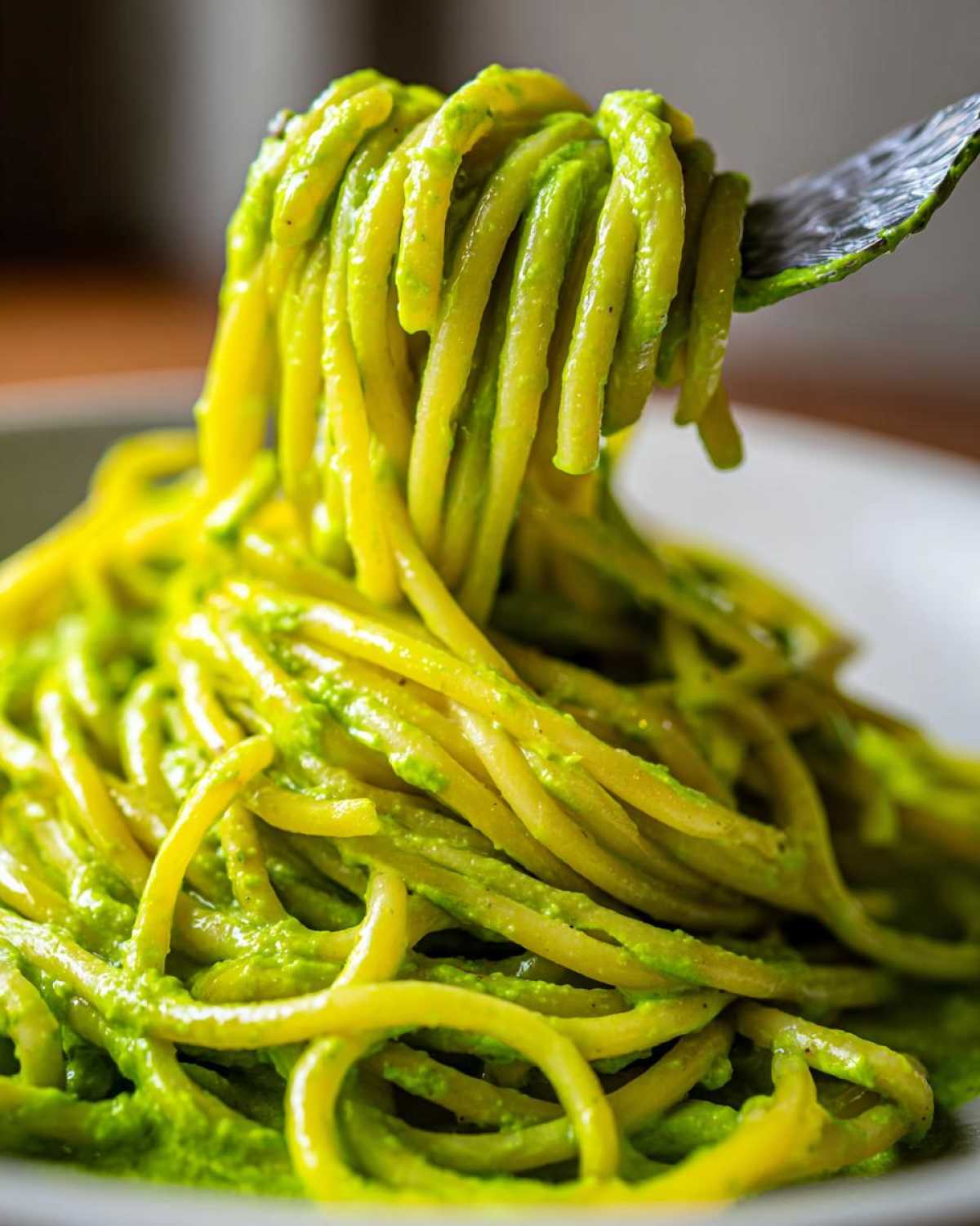 A fork lifts a generous twirl of spaghetti coated in bright green Creamy Avocado Pasta sauce.