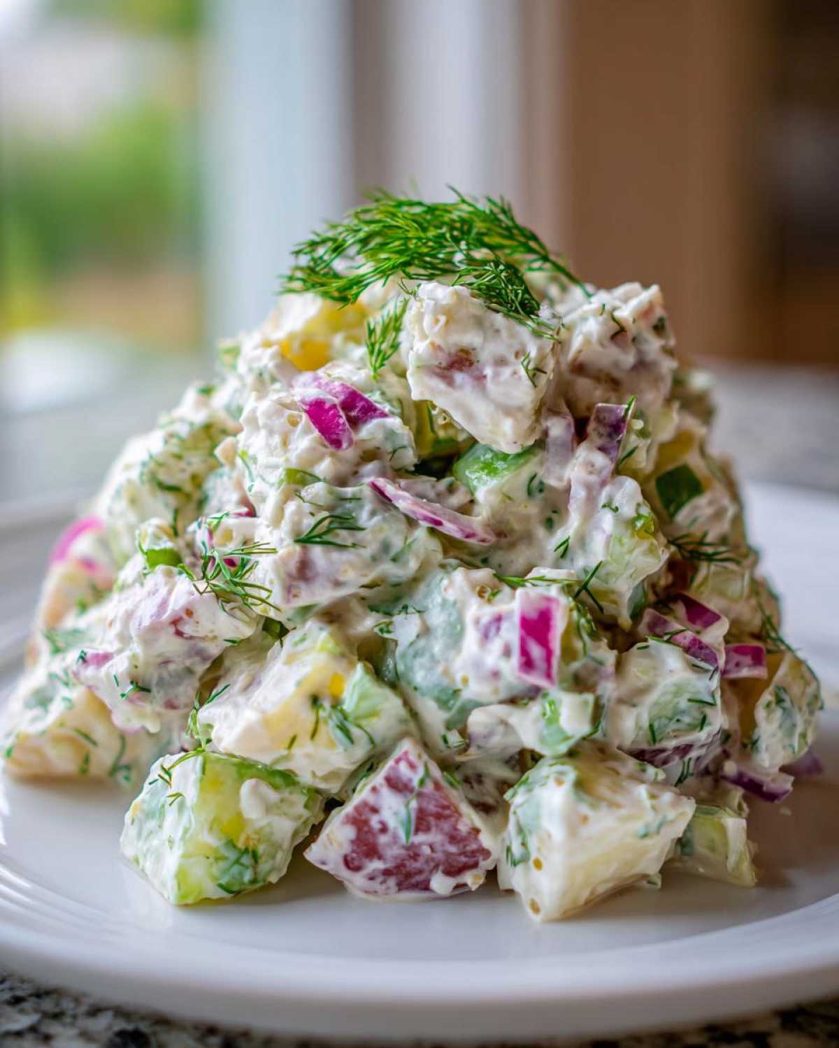 A close-up of a mound of Creamy Dill Potato Salad featuring chunks of potato, red onion, and fresh dill in a creamy dressing.