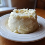 A molded serving of Creamy Garlic Mashed Cauliflower topped with melted butter on a white plate.