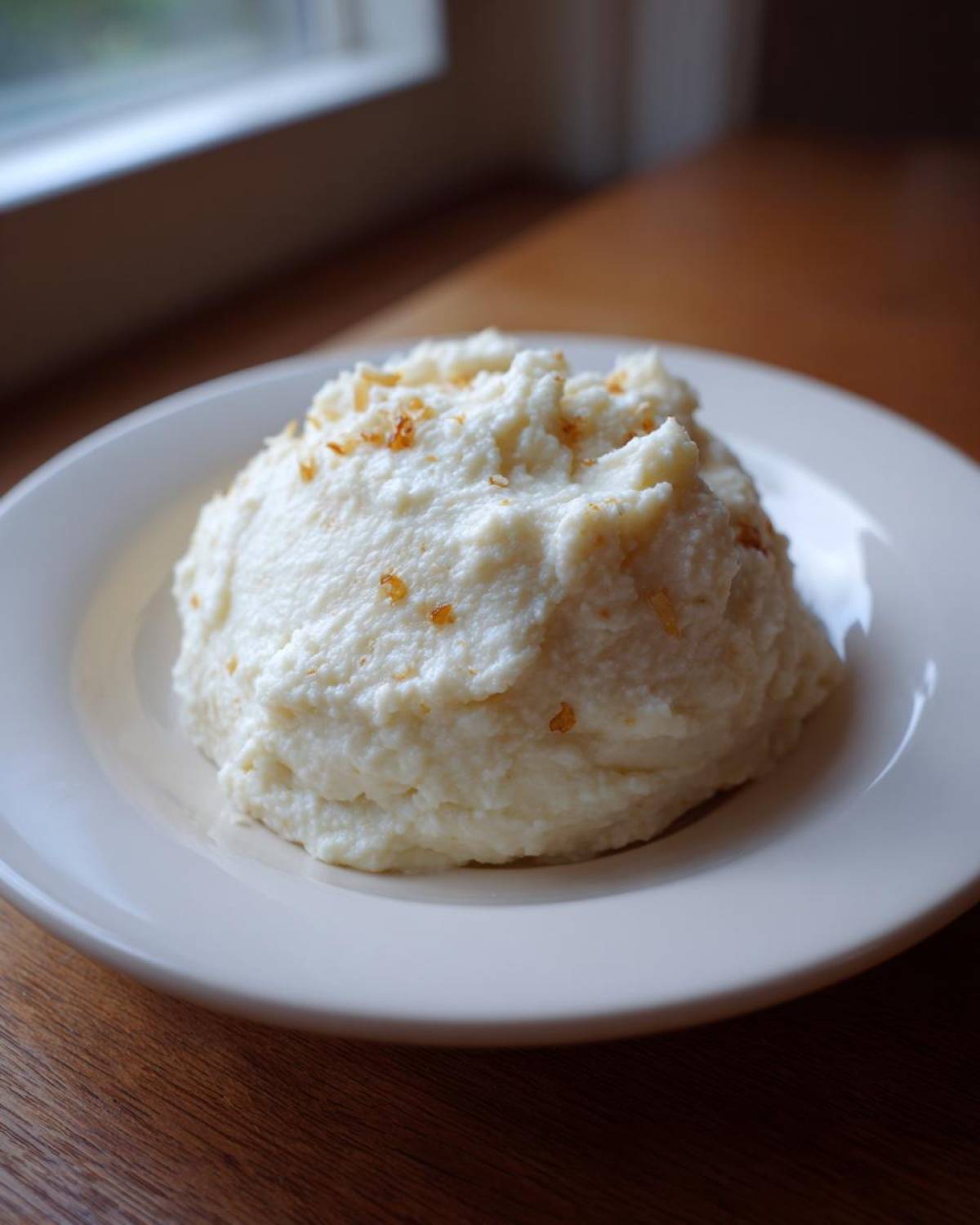 A mound of fluffy Creamy Garlic Mashed Cauliflower topped with browned garlic bits on a white plate.