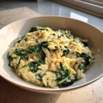 Close-up of a white bowl filled with Creamy Garlic Parmesan Orzo with Spinach, coated in a rich, white sauce.
