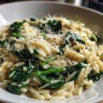Close-up of a white bowl filled with Creamy Garlic Parmesan Orzo with Spinach, topped with grated cheese.
