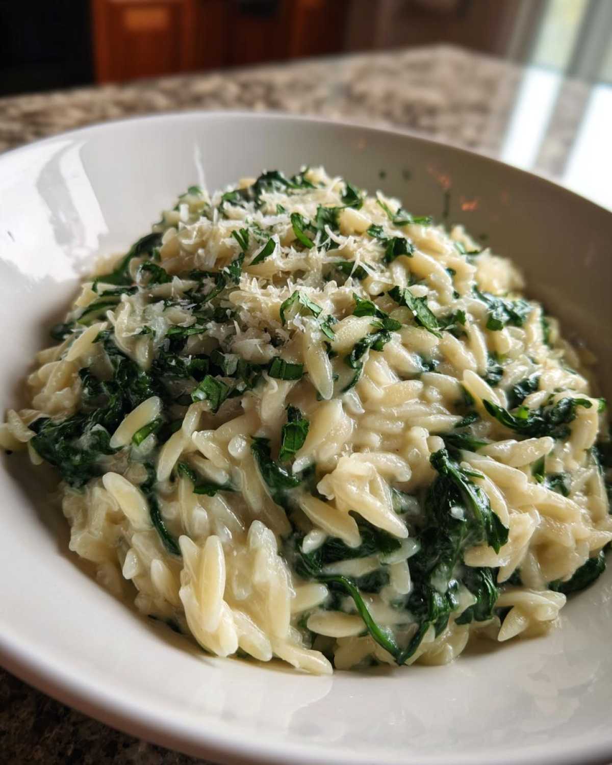 A close-up of a bowl filled with Creamy Garlic Parmesan Orzo with Spinach, topped with grated cheese.