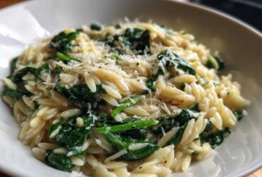 Close-up of a white bowl filled with Creamy Garlic Parmesan Orzo with Spinach, topped with grated cheese.