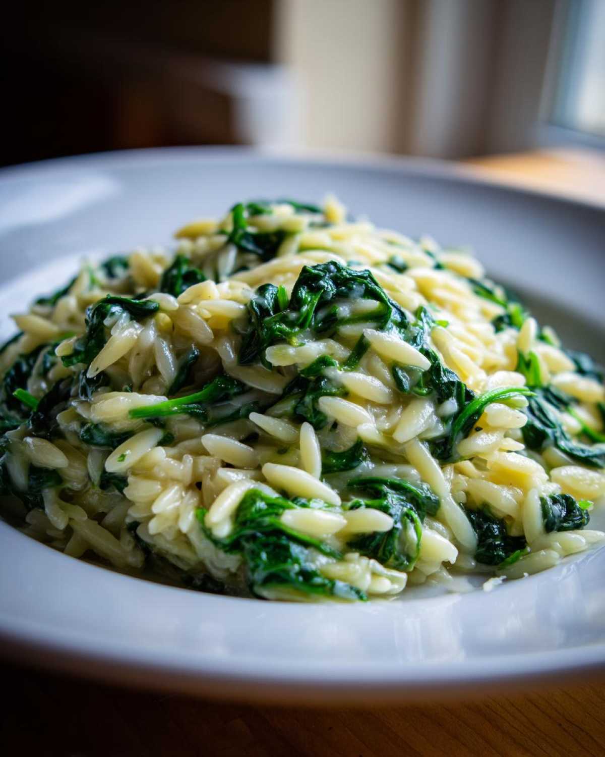 Close-up of a serving of Creamy Garlic Parmesan Orzo with Spinach in a white bowl.