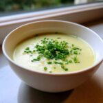 A close-up of a white bowl filled with smooth, creamy potato leek soup, topped generously with fresh chopped chives.