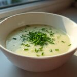 A close-up of a bowl of smooth Creamy Potato Leek Soup topped generously with fresh chopped chives and black pepper.